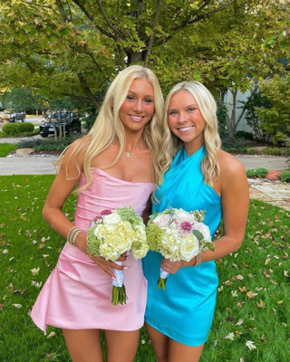 Two girls wearing pink and blue homecoming dresses, holding floral bouquets. 
